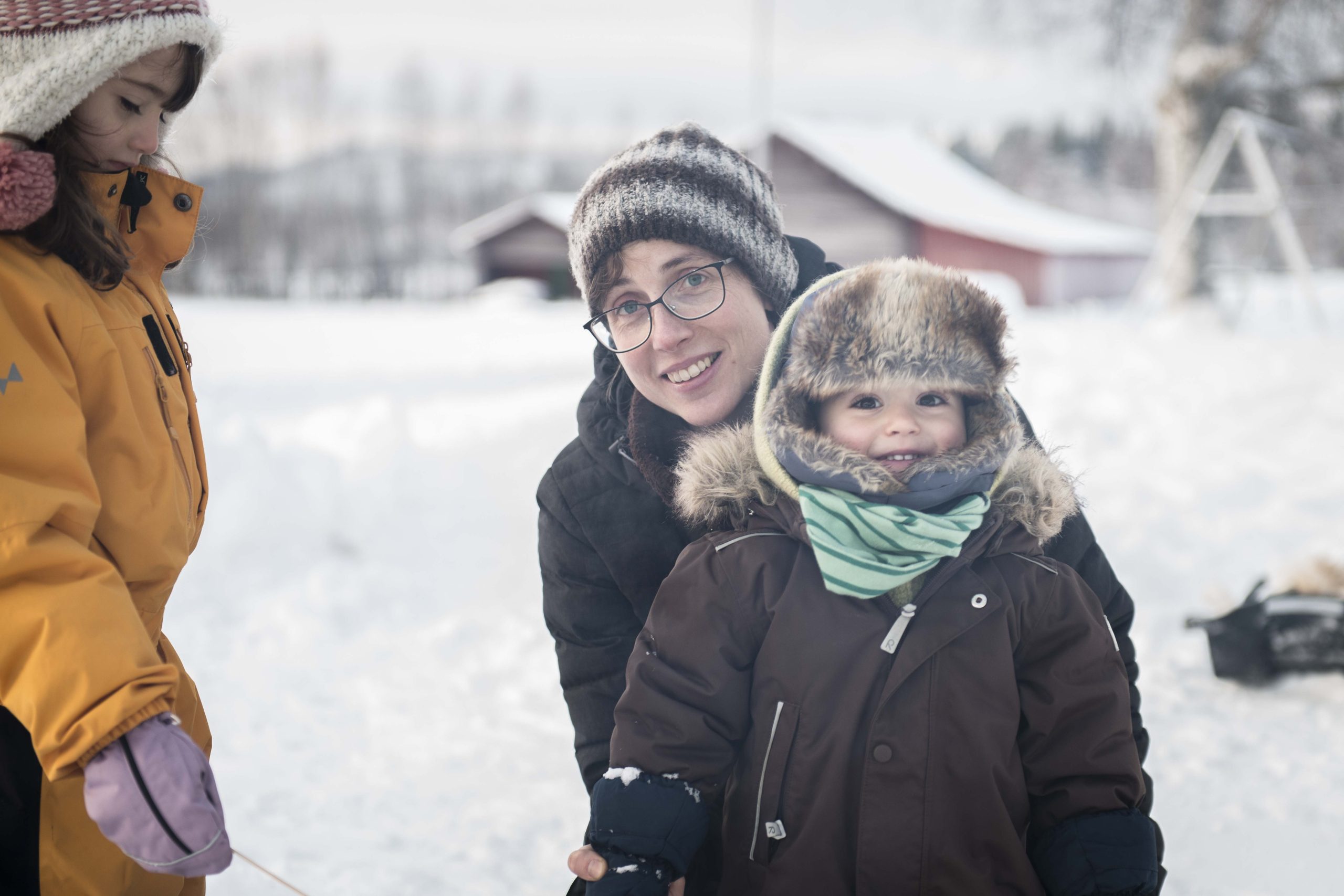 Linnea tittar in i kameran bakom ett vinterklätt barn i pälsmössa.